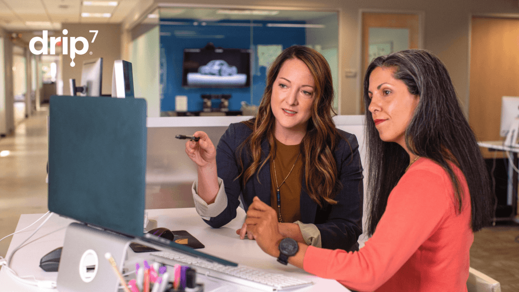 Two women talking and looking at a desktop comptur. 
