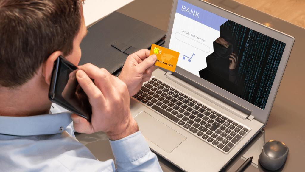 A man looks at a credit card, while on the phone and with a laptop.